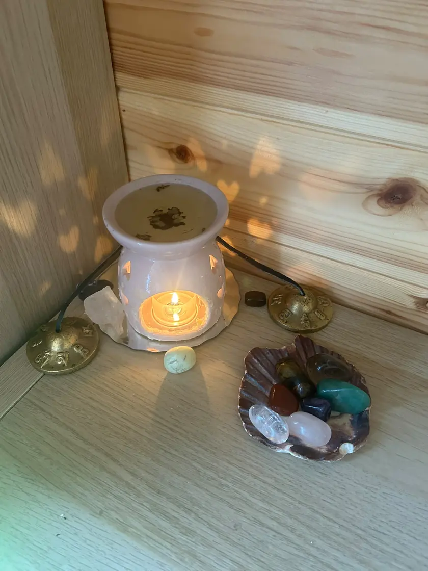 An oil burner glowing on a pine shelf in the treatment room, with crystals in a shell and little heart-shaped patches of light on the wall