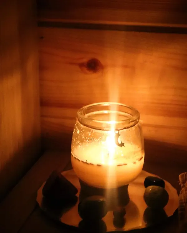 A candle glowing in a jar on a dish of crystals