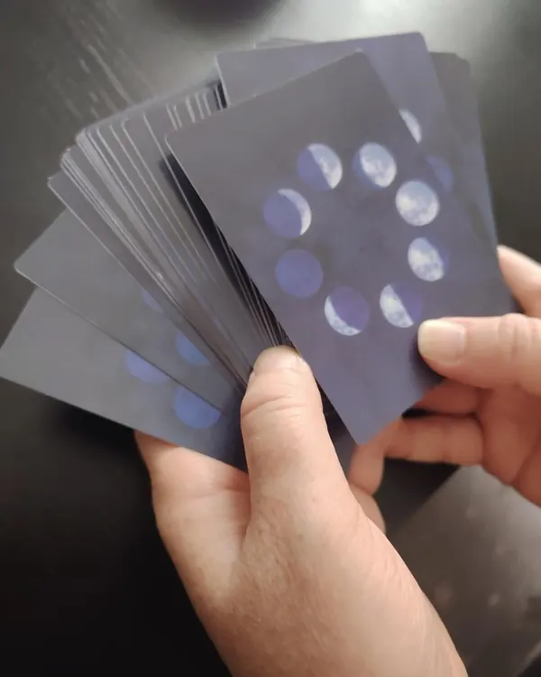 A hand holding a fan of guidance cards with moon-phase backs