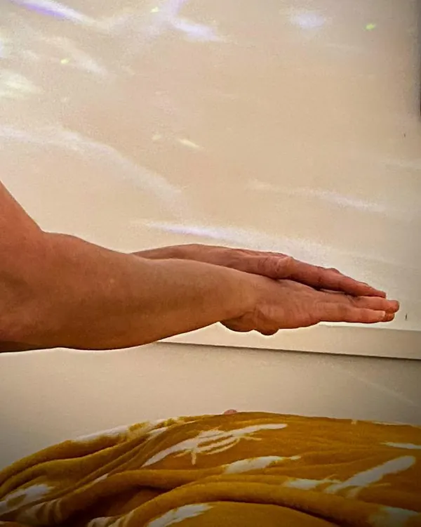 Hands held just above a client wrapped in a yellow blanket, giving reiki